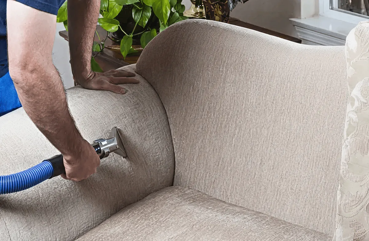 Professional upholstery cleaner deep-cleaning a fabric sofa with a handheld extraction tool and hose, Cleveland, OH.